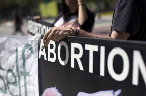 Mujer con un rosario sobre un rótulo que dice aborto en inglés